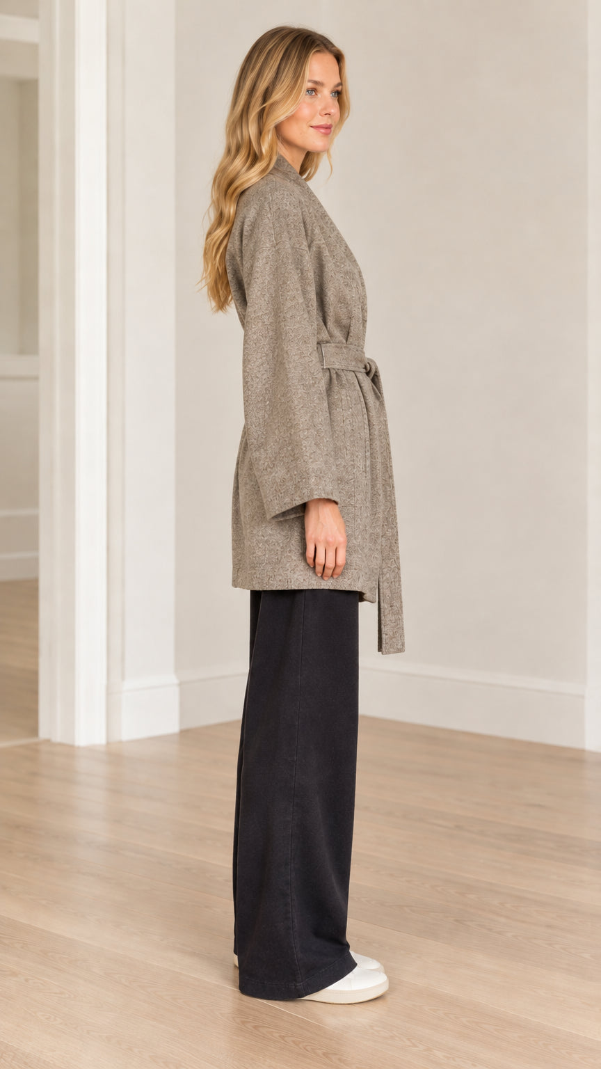 Side profile view of model wearing taupe herringbone belted coat showing mid-thigh length and wide sleeve
