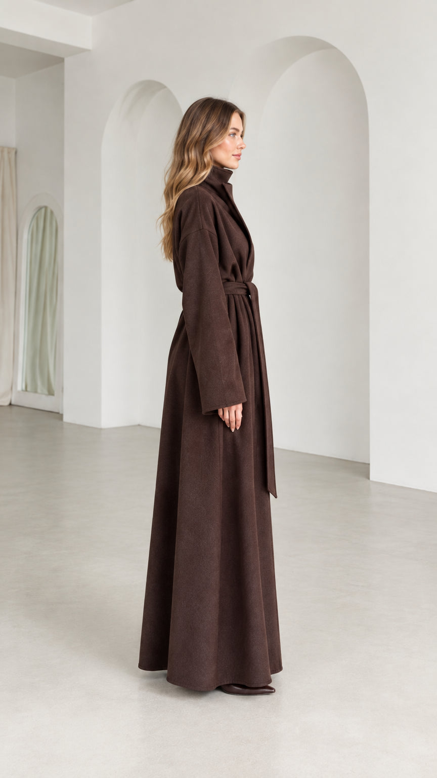 Side profile view of model wearing long brown belted wrap coat