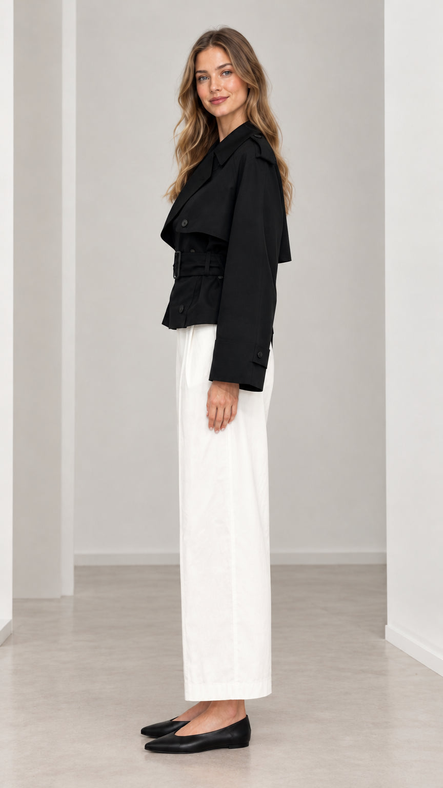 Side profile view of woman wearing black cropped belted trench jacket with wide sleeves