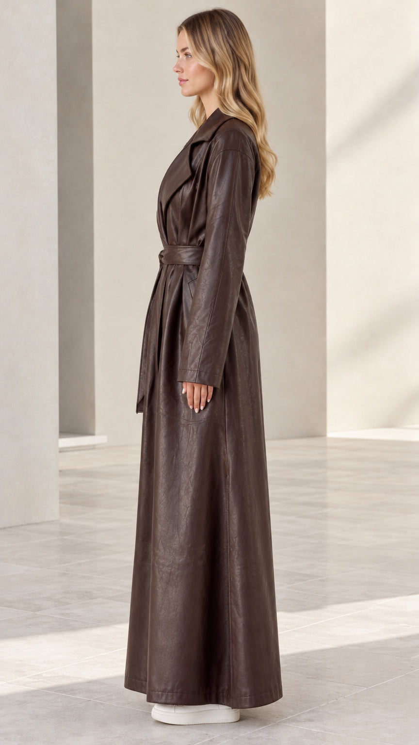 Side profile view of woman wearing full-length brown faux leather trench coat