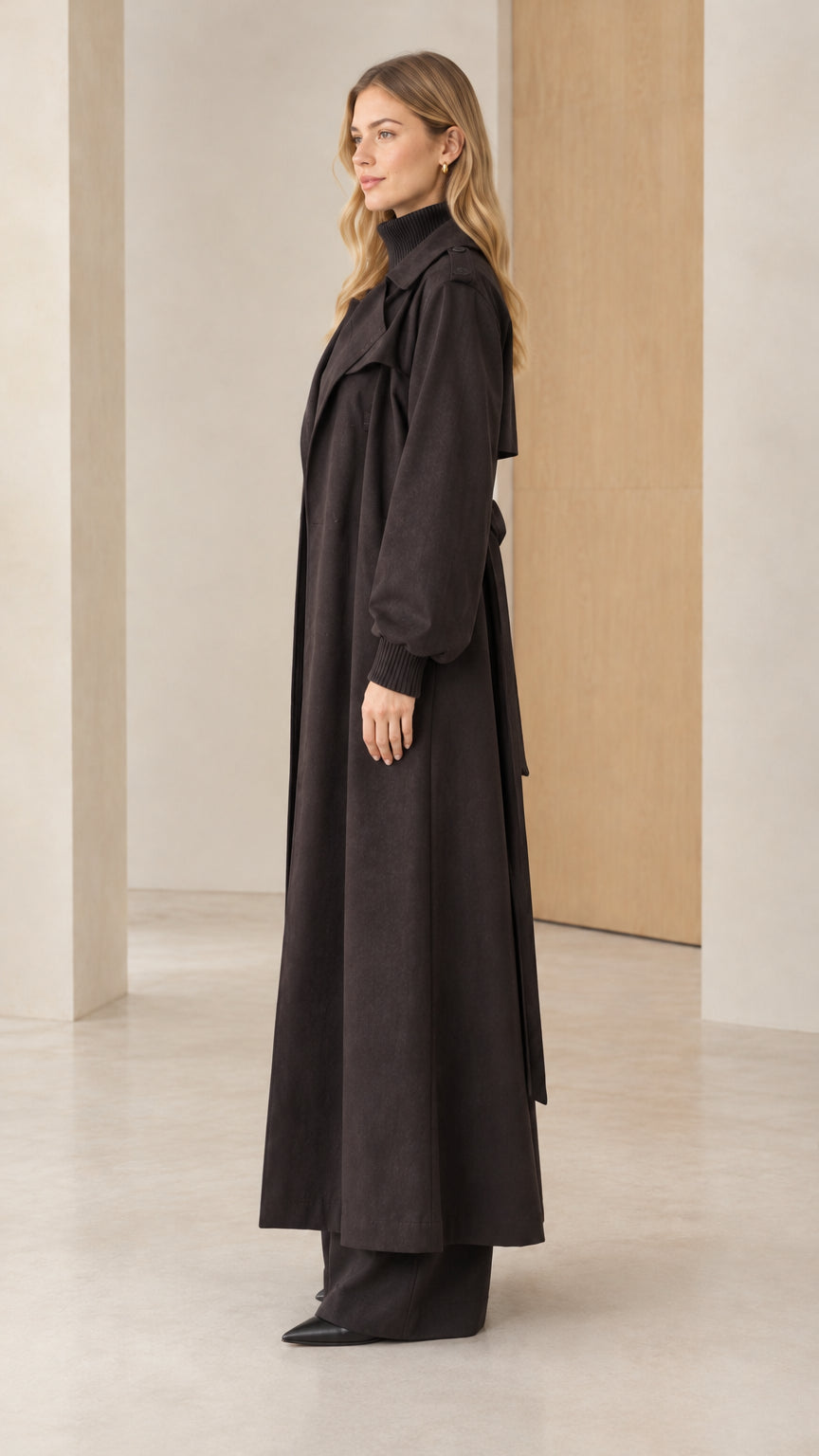 Side profile view of woman modeling black ankle length trench coat