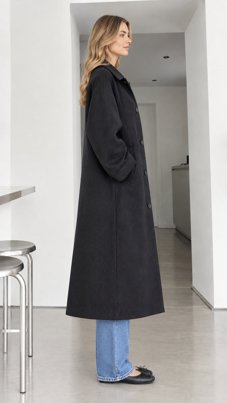 Side profile view of black longline button-front overcoat showing relaxed drape
