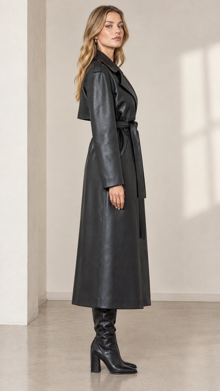 Side profile view of woman wearing long black faux leather trench coat
