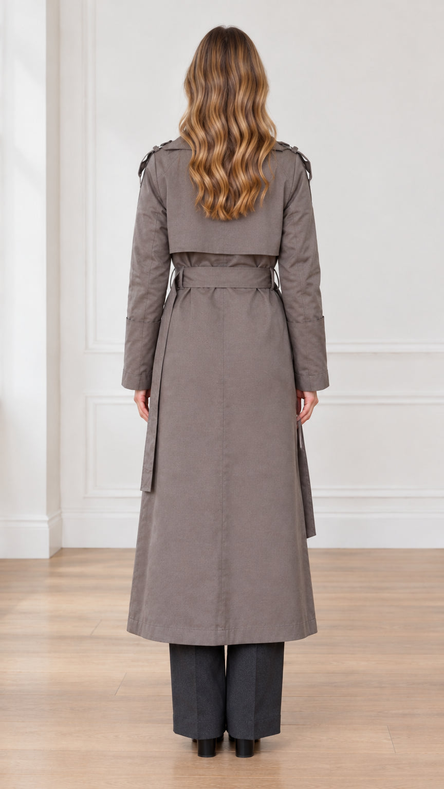 Back view of woman wearing taupe maxi trench coat showing back storm flap and belt