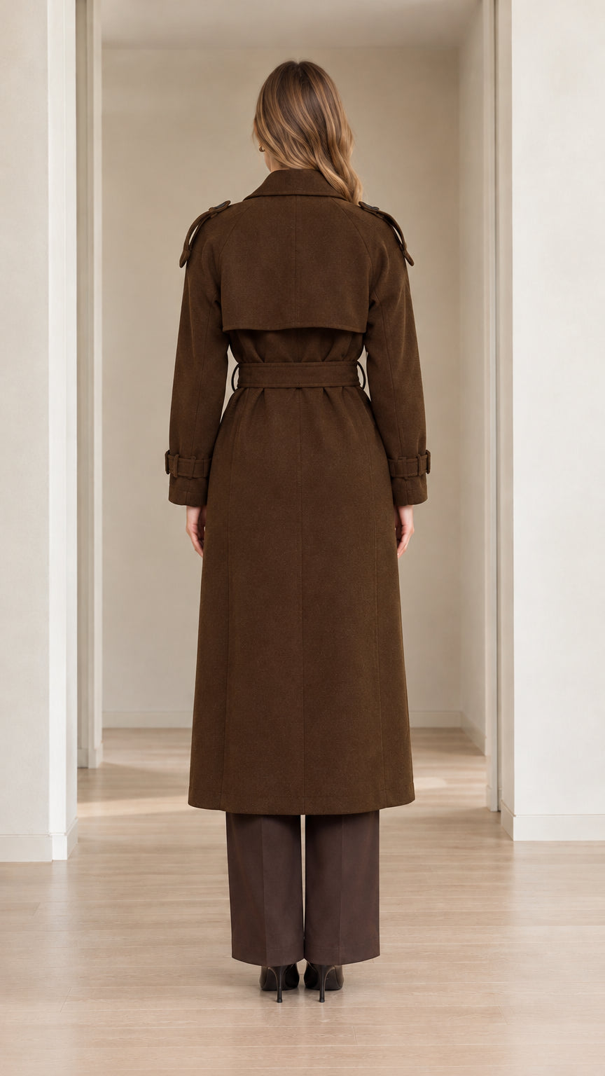 Back view of model wearing brown long trench coat showing storm flap and belt