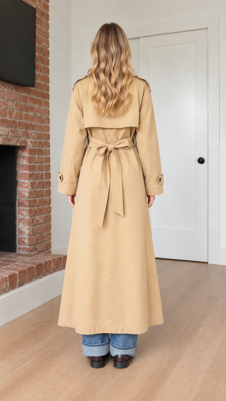 Back view of model wearing camel belted trench coat showing rear flap and tied belt
