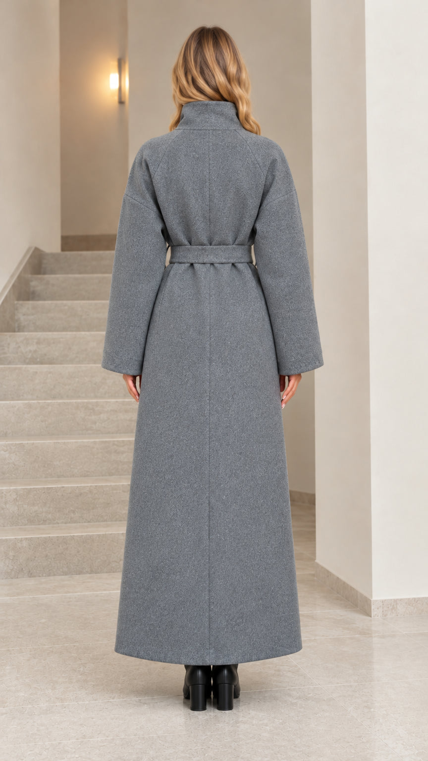 Back full-length view of woman wearing grey high collar belted maxi overcoat