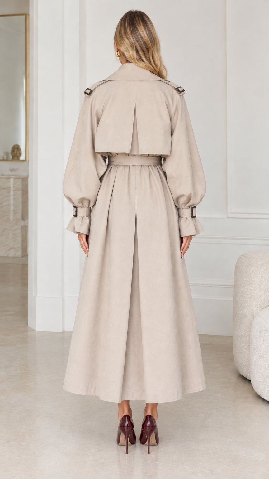 Back view of woman wearing ankle-length beige trench coat showing back storm flap and pleat