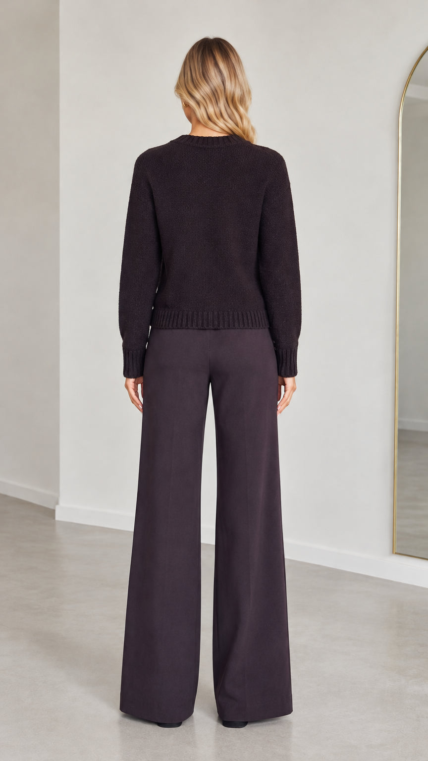 Back view of model wearing Dark Plum knit cardigan and wide-leg trousers