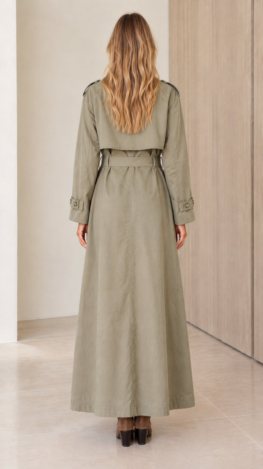 Back view of a model wearing a sage green longline trench coat showing the storm flap and belted waist