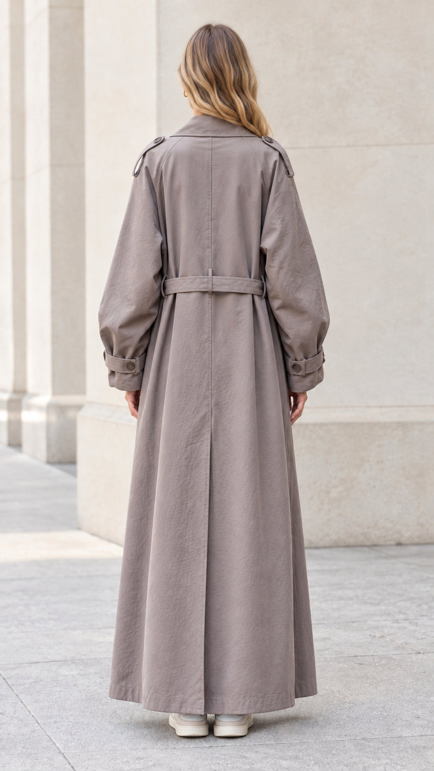 Back view of taupe maxi trench coat showing back storm flap and tie belt