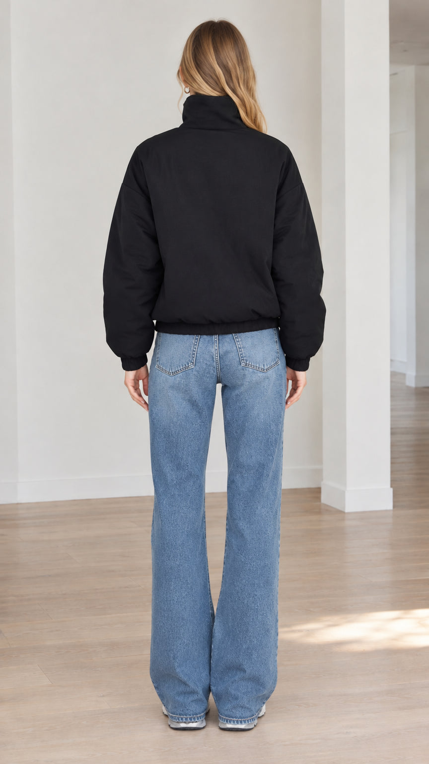 Back view of model wearing black padded jacket with elasticated hemline and jeans
