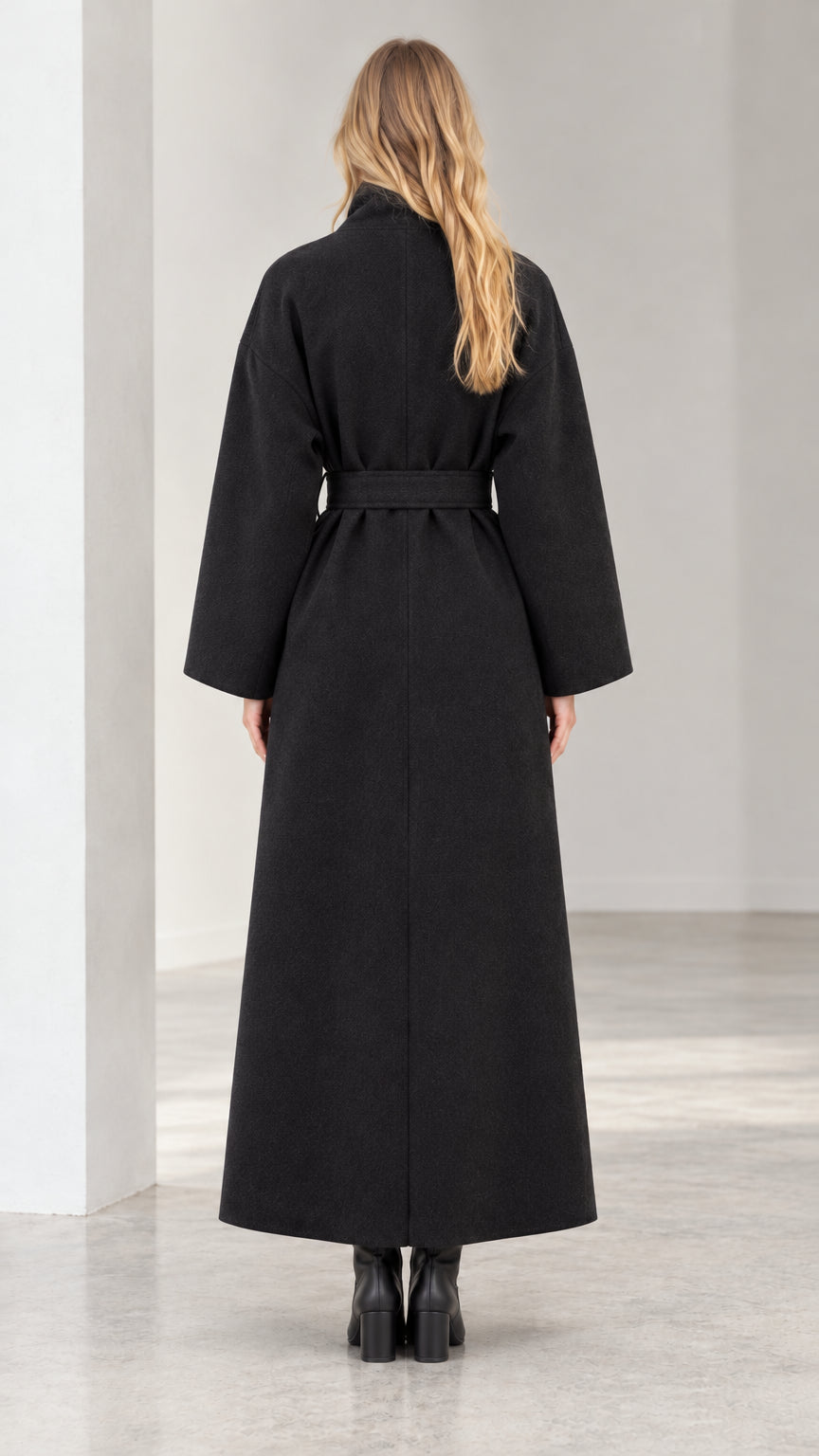 Back view of woman wearing long black belted overcoat showing streamlined fit