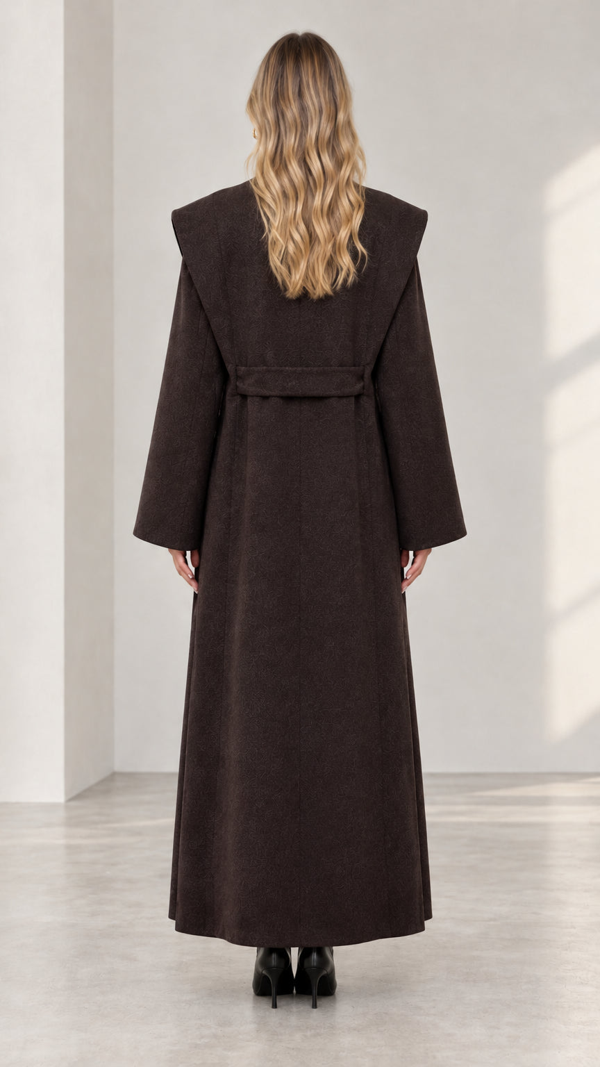 Back view of woman wearing full length dark brown overcoat with waist tie
