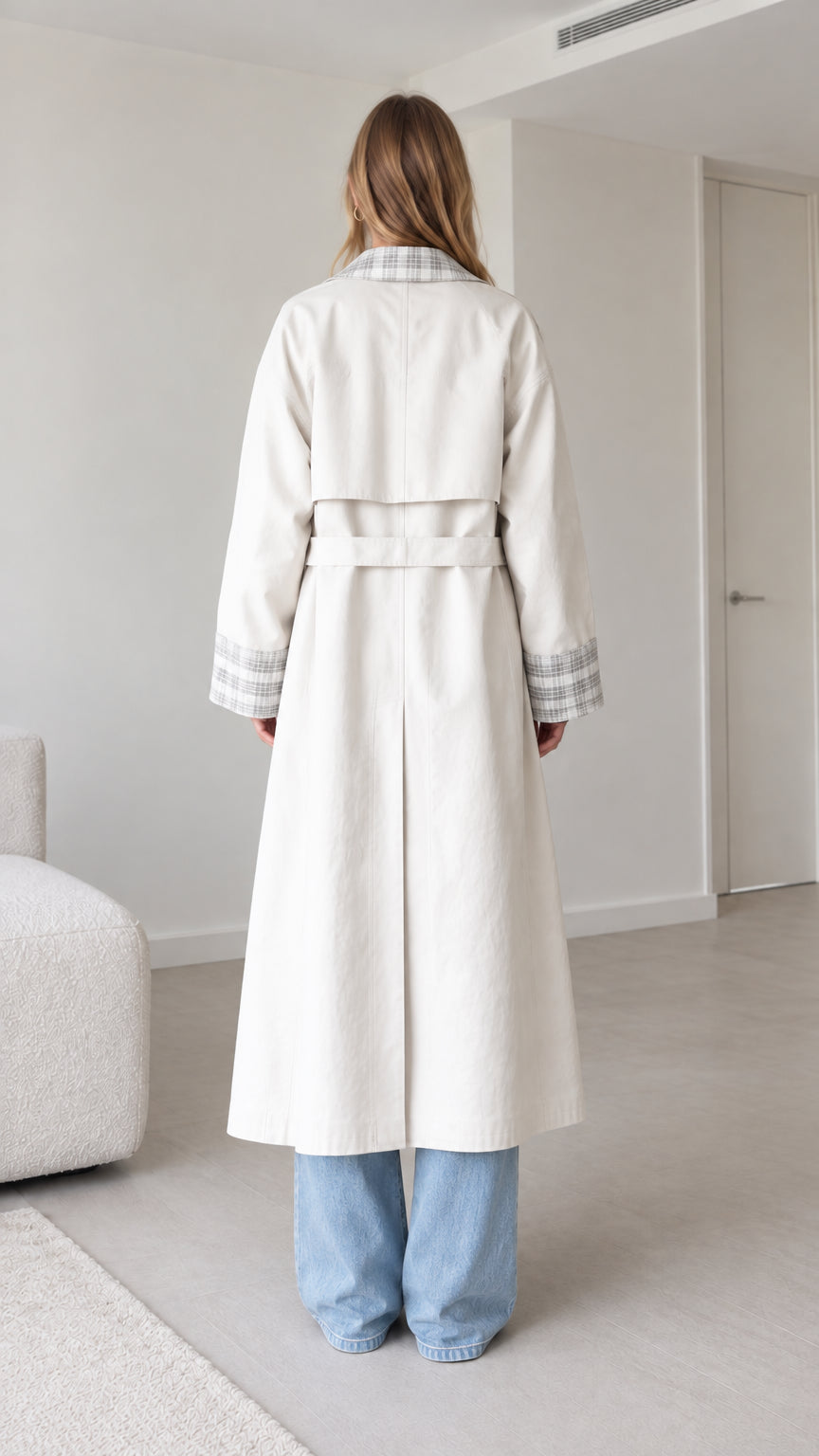 Back full-length view of woman wearing belted off-white trench coat with storm flap