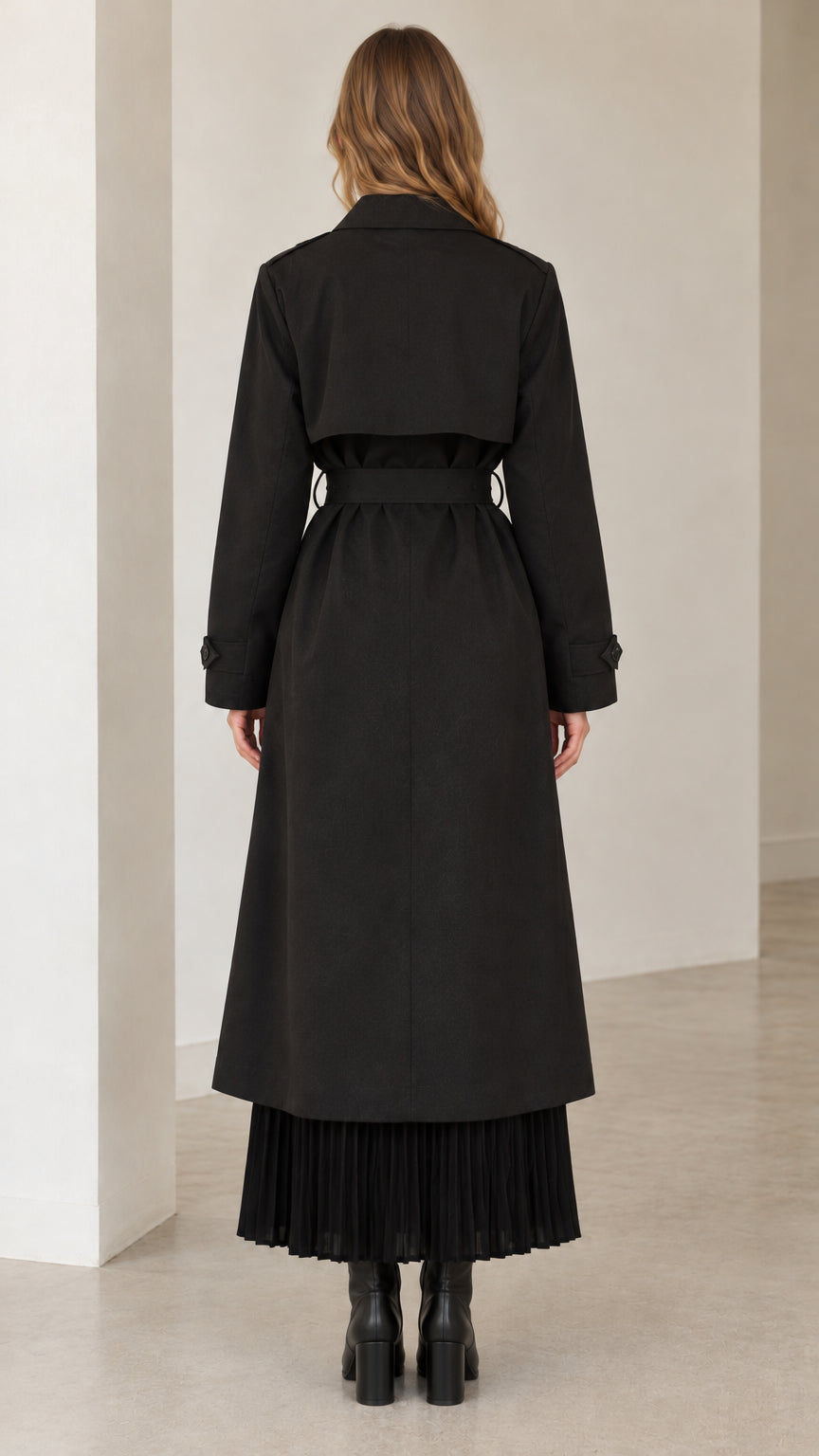 Back view of model wearing long black belted trench coat showing back storm flap