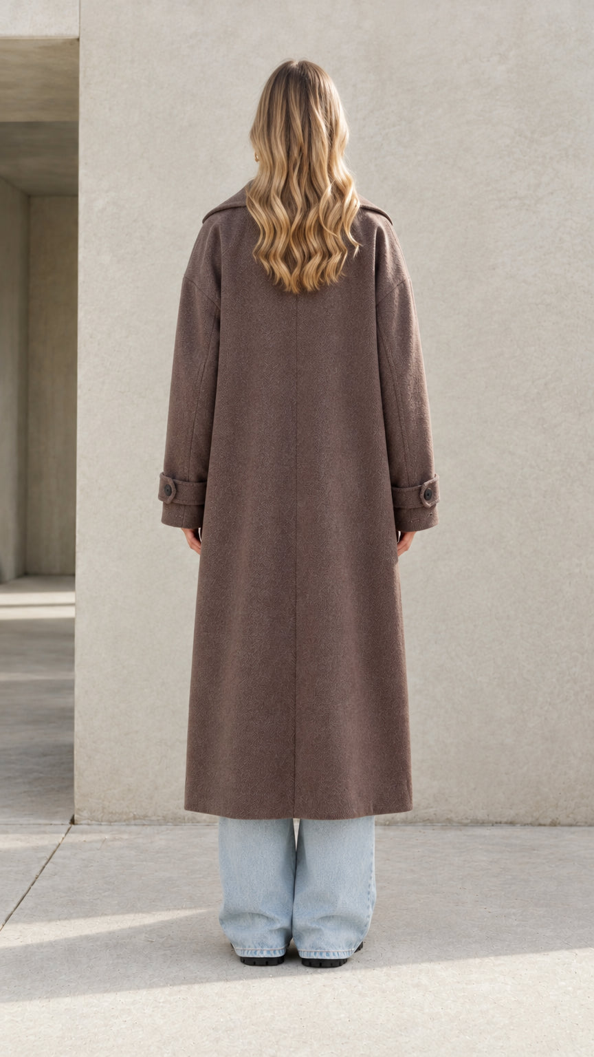 Back view of model wearing brown long overcoat highlighting clean silhouette