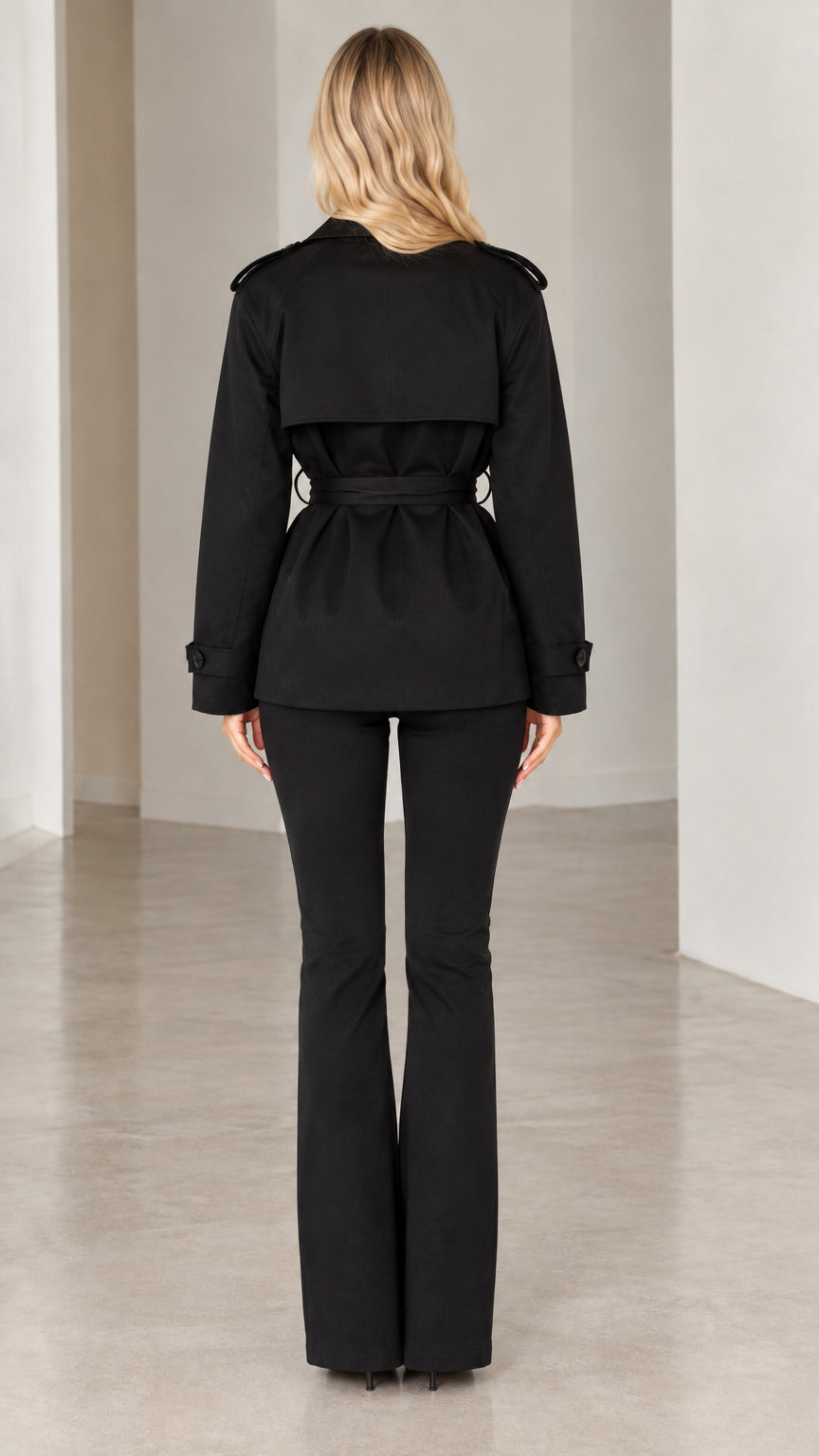 Back view of model showing trench jacket storm flap and flare trouser silhouette in black