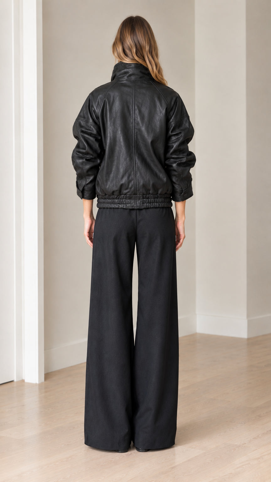 Back view of model in black faux leather bomber jacket and relaxed-fit trousers