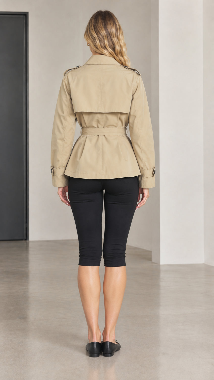 Back view of woman wearing khaki short trench coat showing storm flap detail