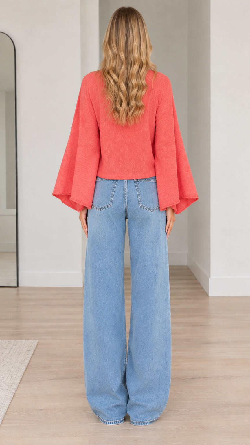 Back view of model showing flared bell sleeves and cropped hem of coral cardigan