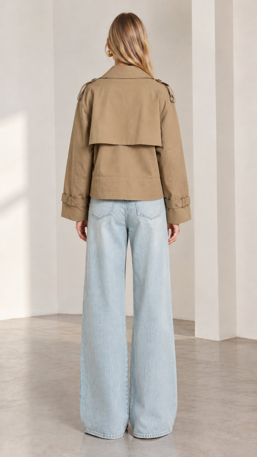 Back full-length view of model wearing khaki cropped trench jacket showing back storm flap detail