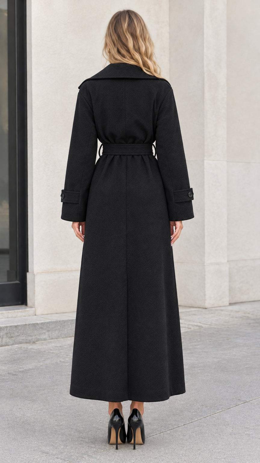 Back view of woman wearing ankle-length black coat tied with fabric belt