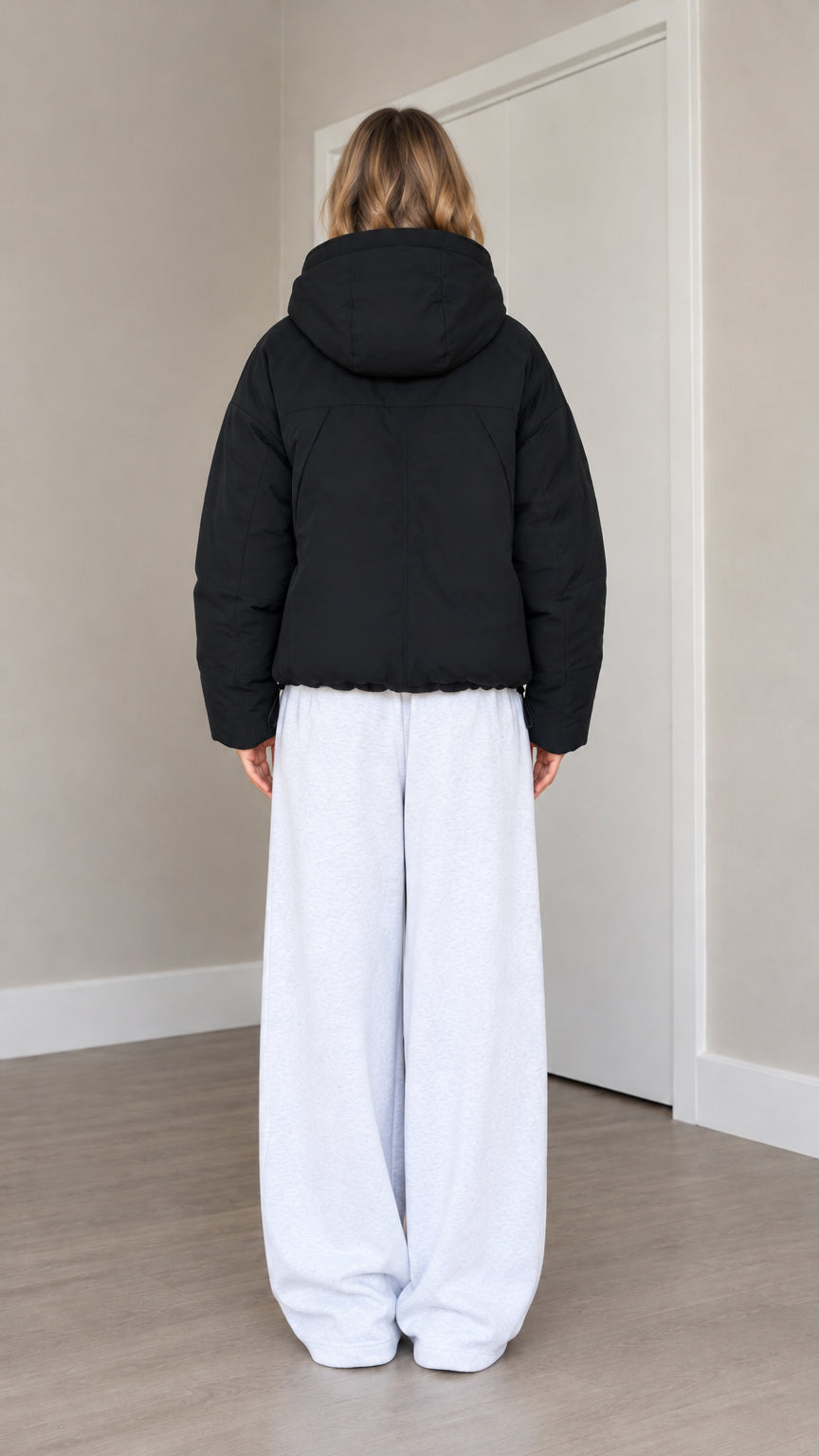 Back view of model wearing black hooded puffer jacket with hood up