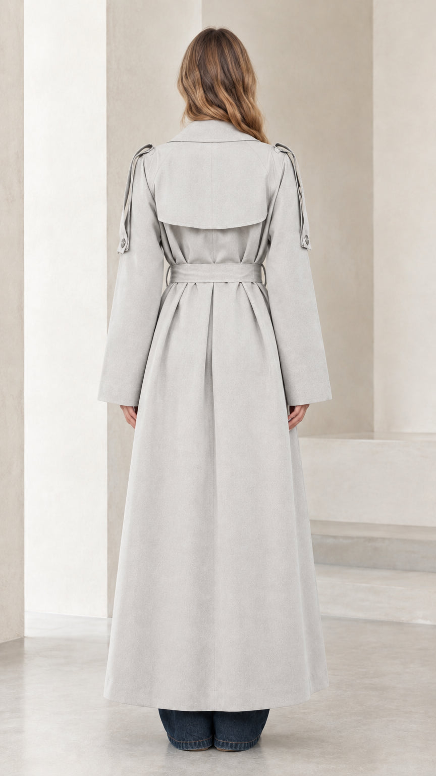 Back view of model showing back storm flap and draped hem of light grey maxi trench coat