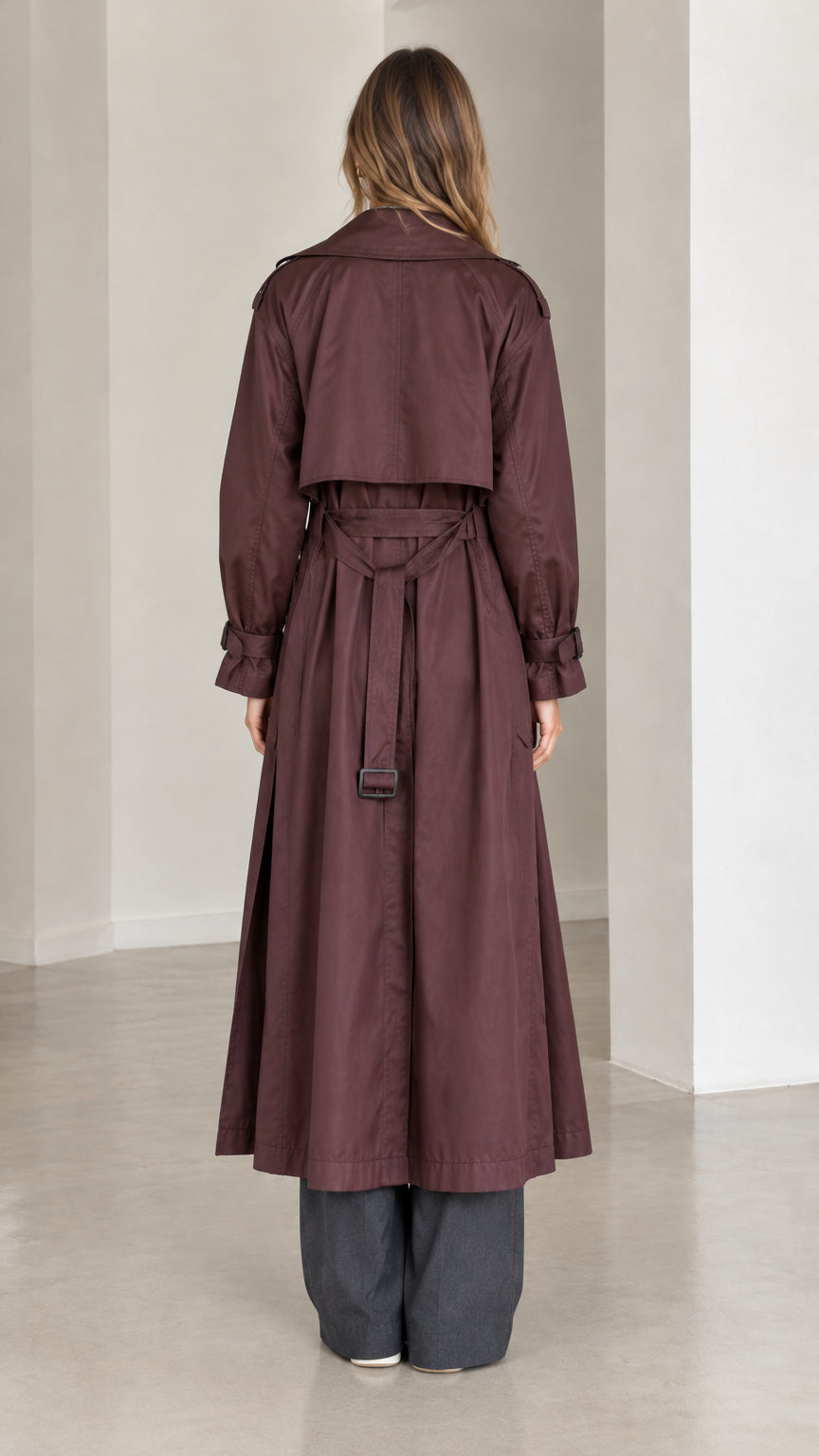 Back view of model wearing burgundy long trench coat showing storm flap and belt