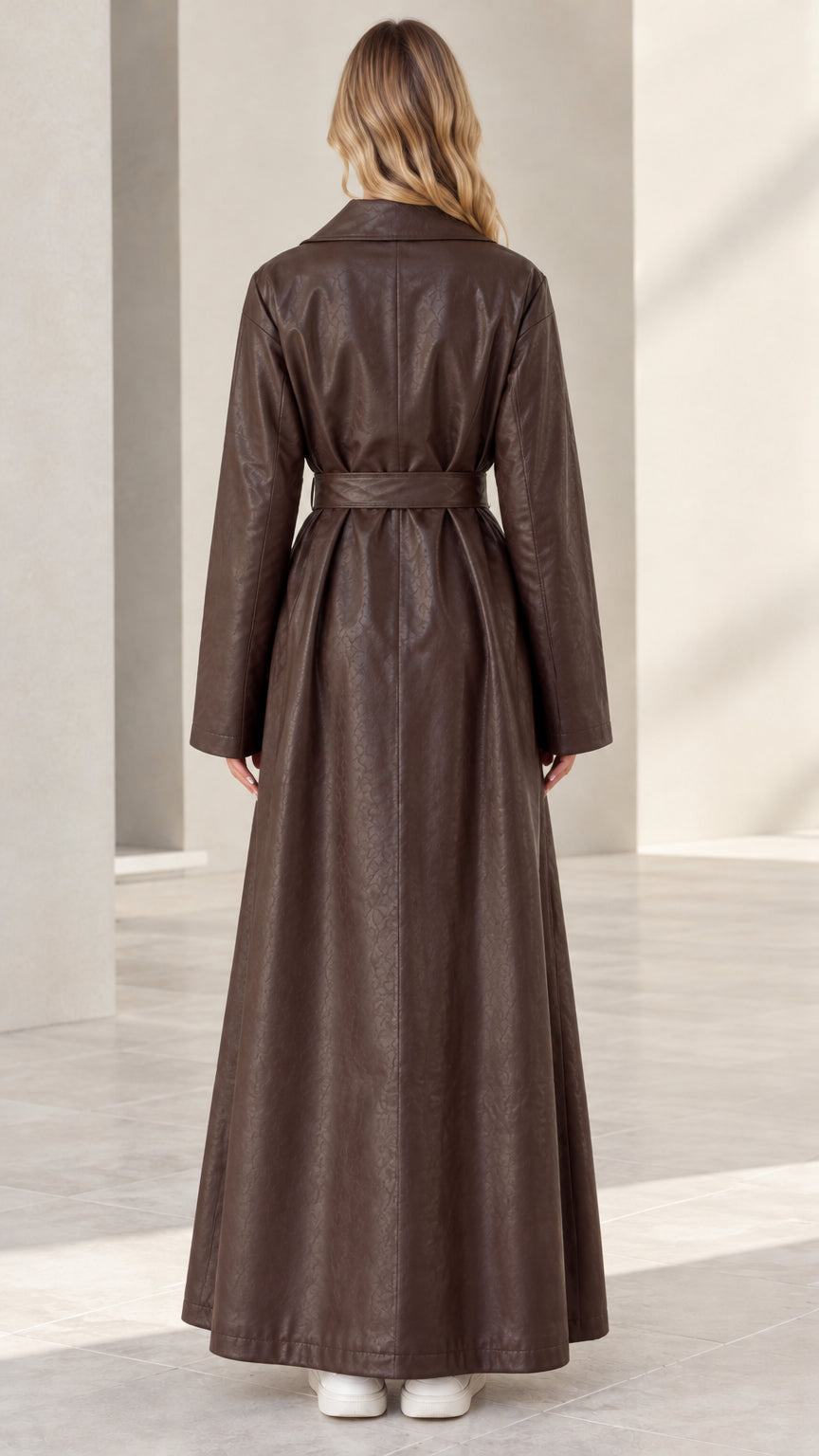 Back full-length view of woman in brown faux leather maxi trench coat with tie belt