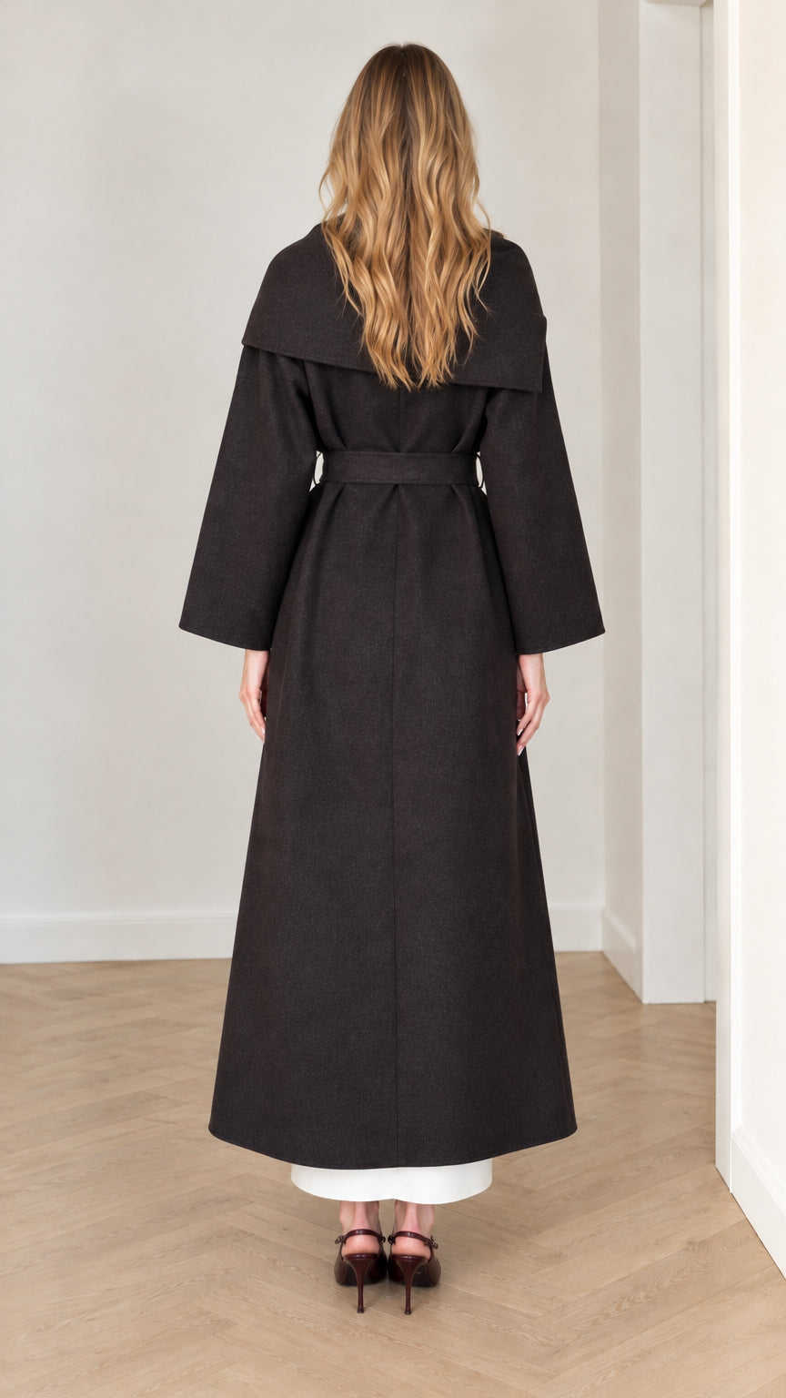 Back view of model wearing full-length black wrap coat with scarf detail