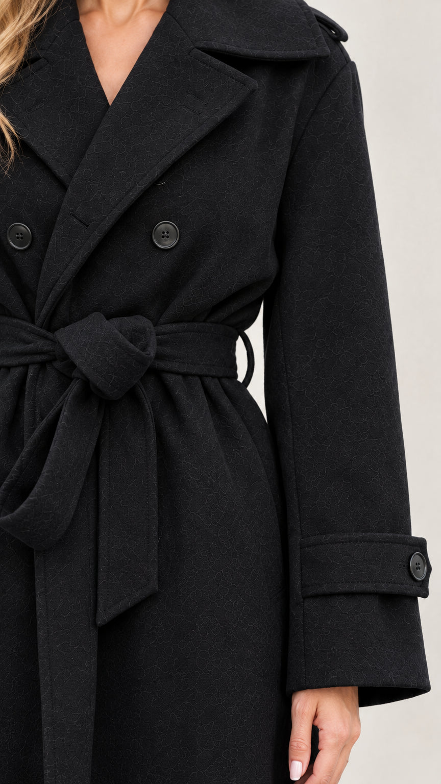 Close-up detail of notched lapel, double buttons, and tie belt on black overcoat
