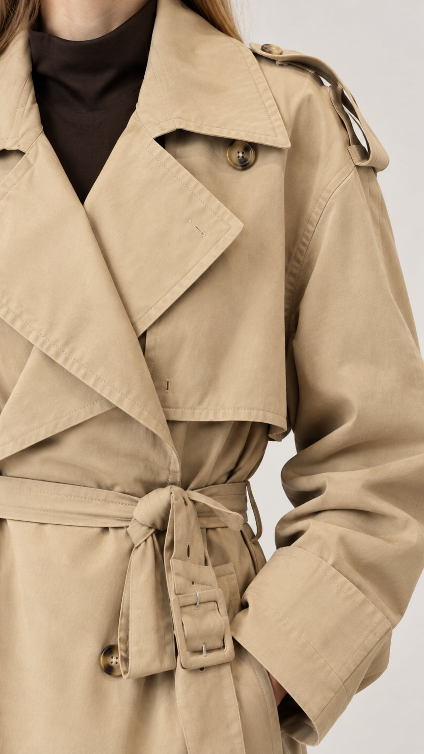 Close-up detail of khaki trench coat collar, shoulder epaulet, buttons, and belt buckle