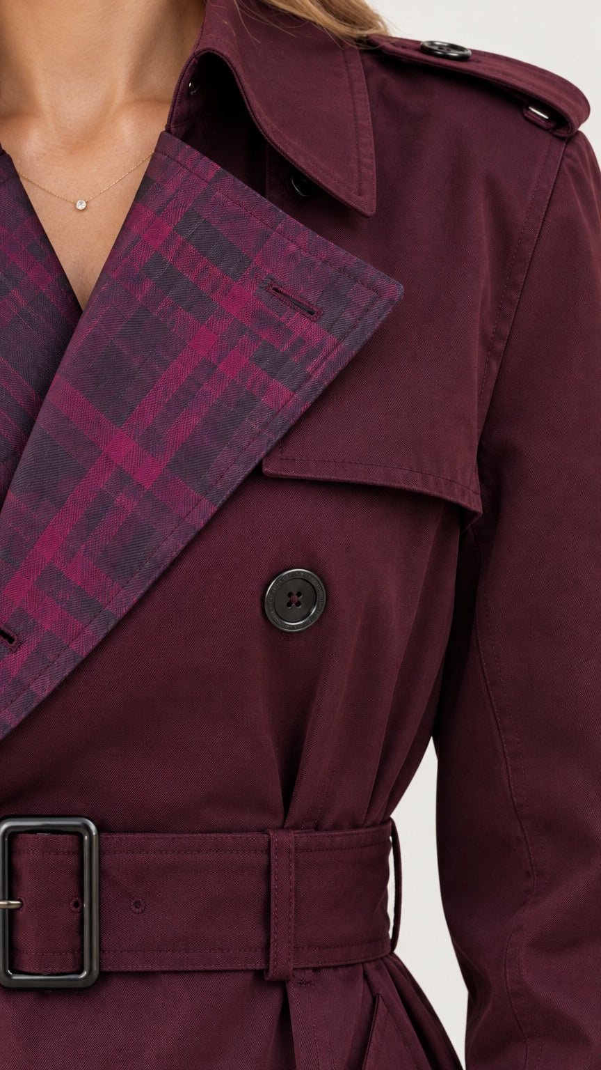 Close-up detail of the burgundy trench coat showing plaid contrast lapel, buttons, and belt buckle