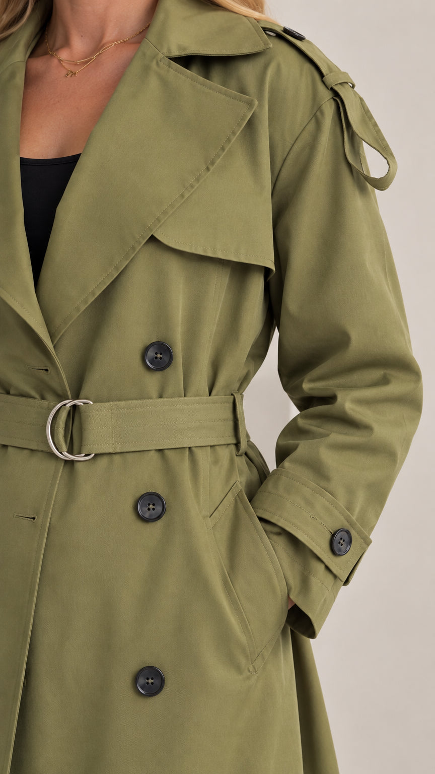 Close-up detail of the olive green trench coat showing notched lapels, buttons, and waist buckle
