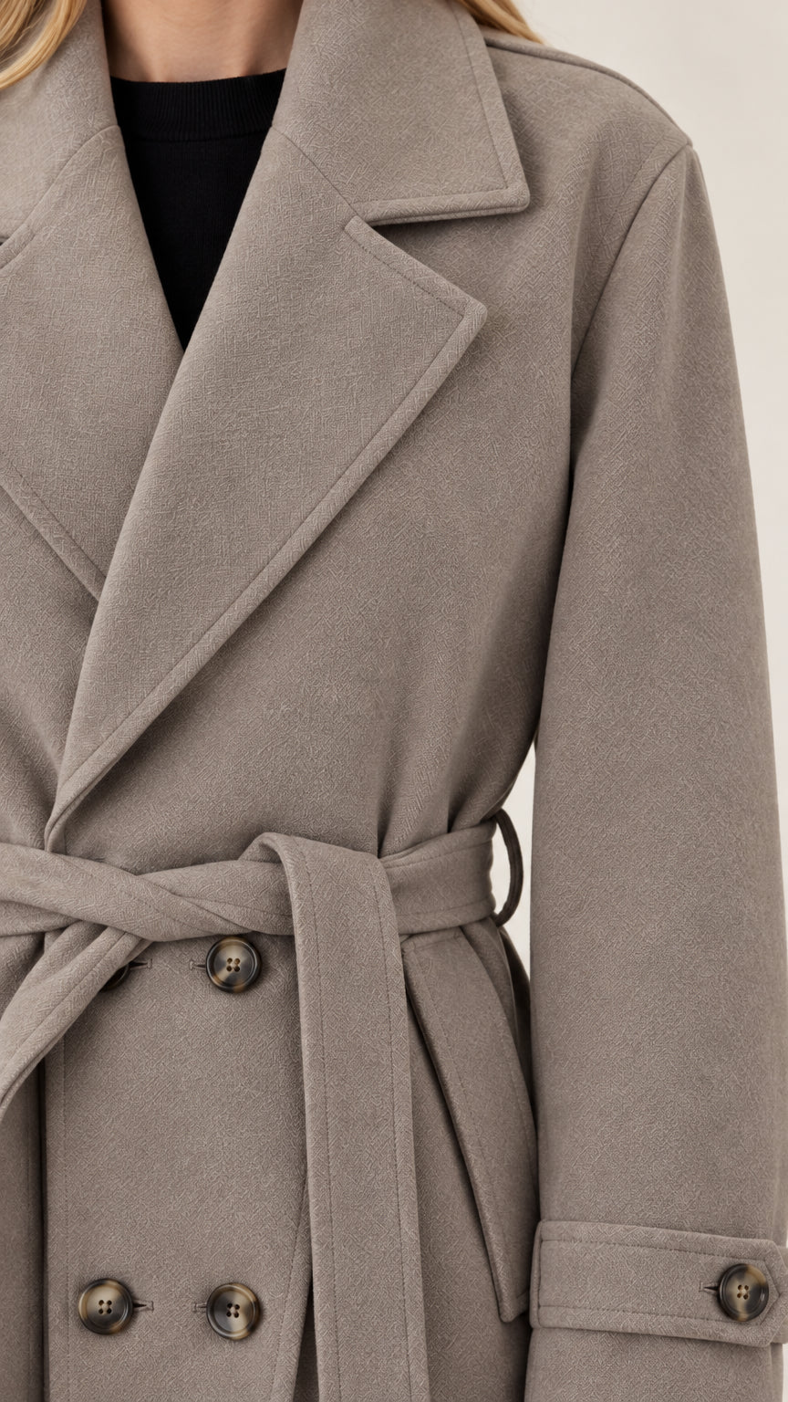 Close-up detail of notched lapels, buttons, and belt texture on taupe overcoat