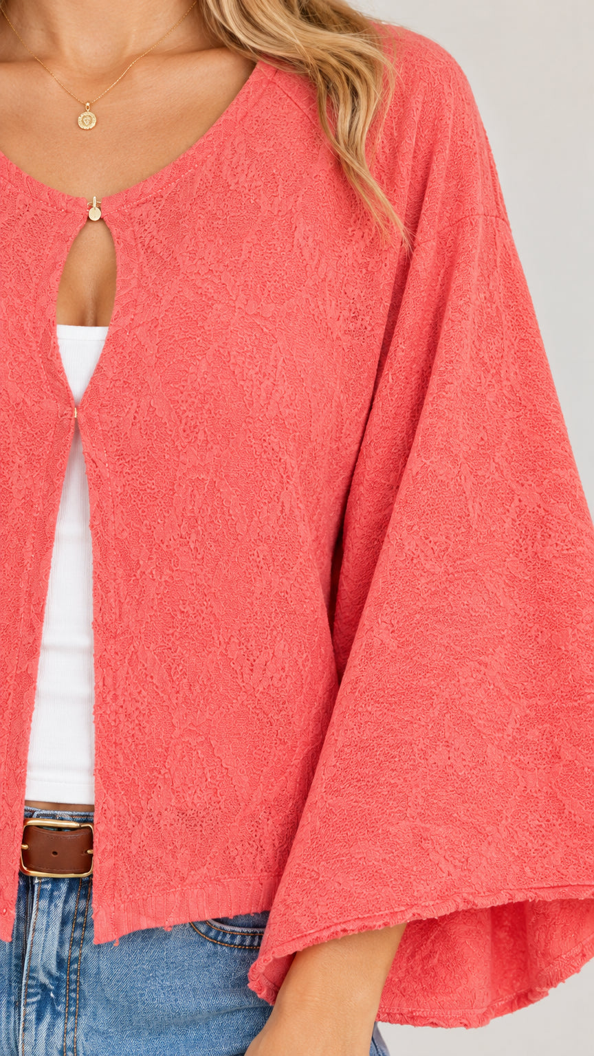 Close-up detail of textured fabric and keyhole button closure on coral cardigan