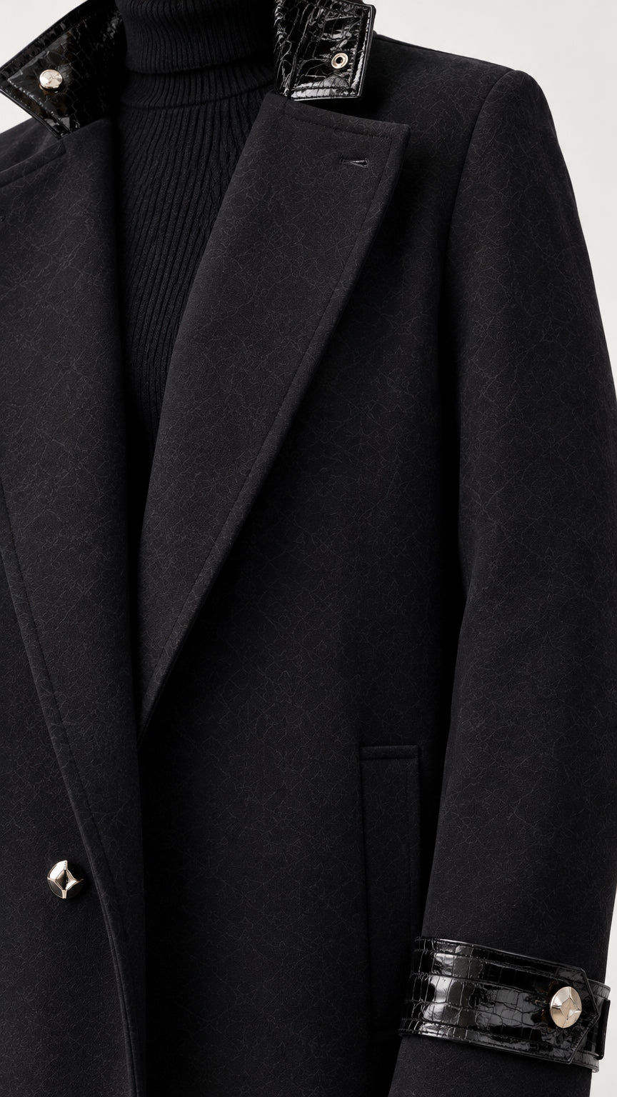 Close-up detail view of black coat showing textured glossy contrast lapel trim, button fastening, and cuff strap detail