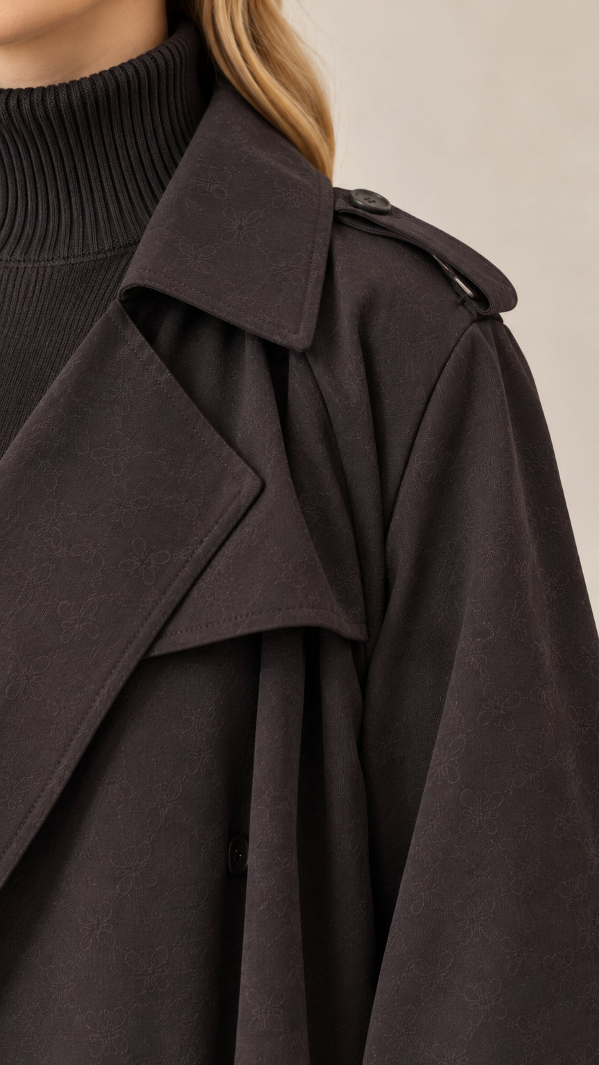 Close-up detail of black maxi trench coat collar, shoulder epaulette, and lapel