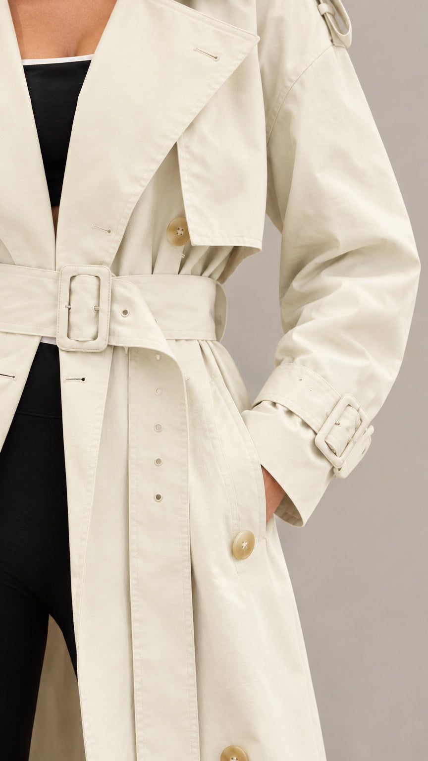 Close-up detail of cream maxi trench coat showing notched lapels, buckle belt, and wrist strap