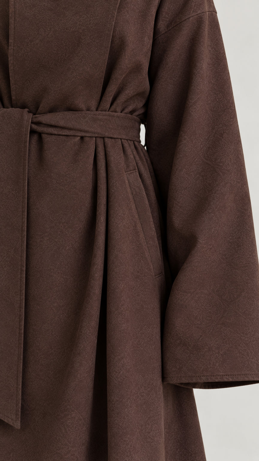 Close up view of brown maxi coat showing belt, fabric texture, and pocket detail