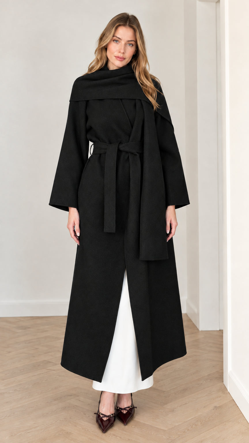 Full-length front view of black belted maxi coat with attached scarf detail