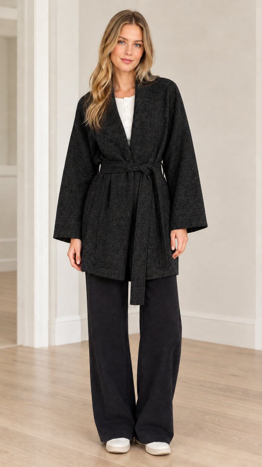 Front view of model wearing black textured herringbone belted wrap coat