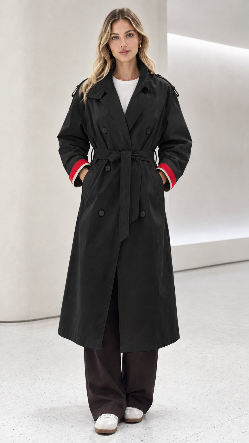 Front view of model wearing black double-breasted trench coat with red contrast cuffs
