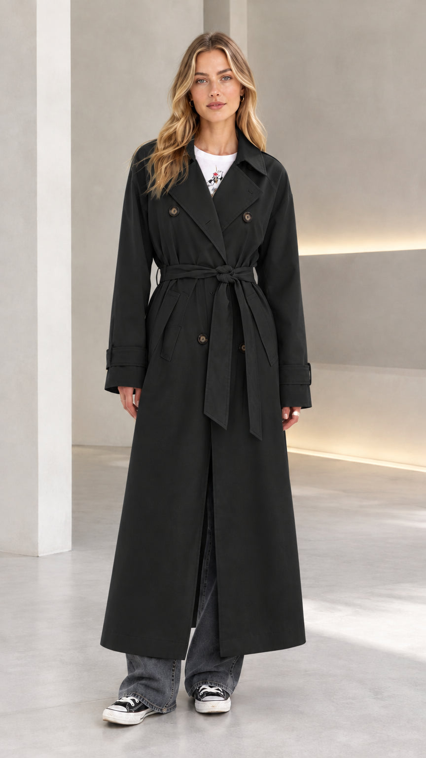 Front view of model wearing black double-breasted long belted trench coat
