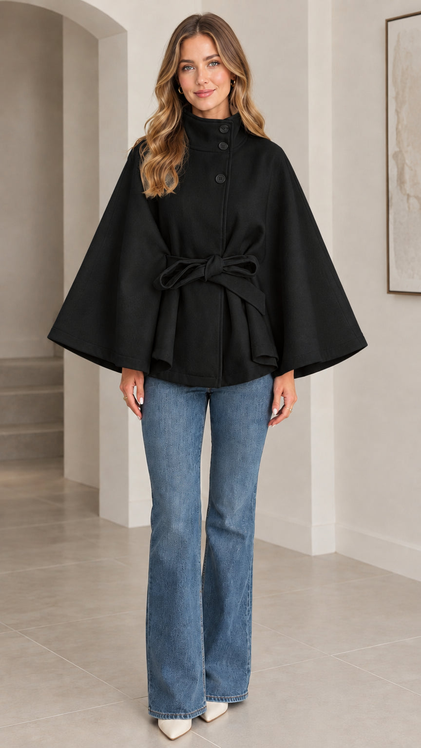 Front view of black high neck belted cape coat styled with denim