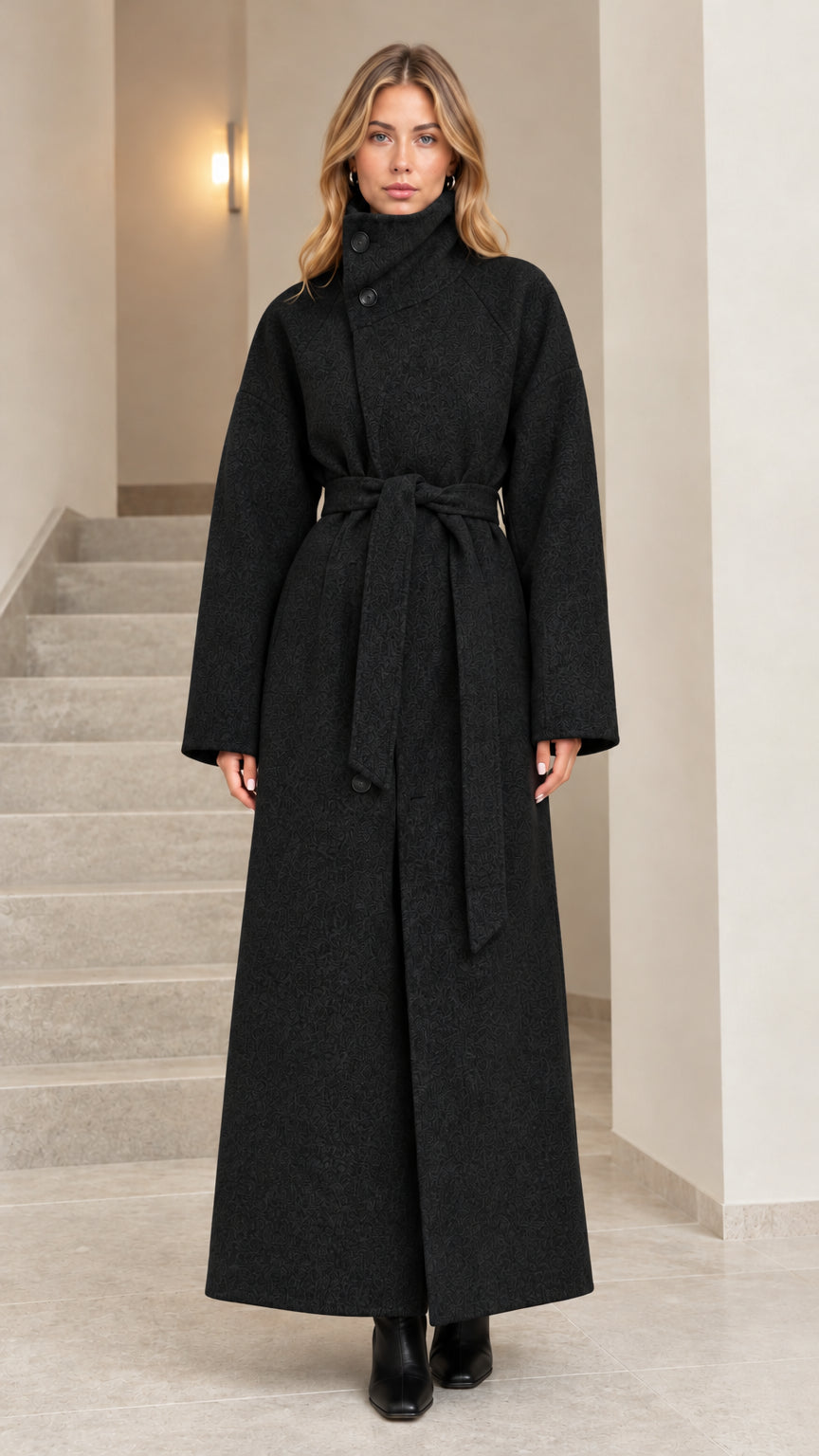 Front view of woman wearing black high collar belted maxi overcoat