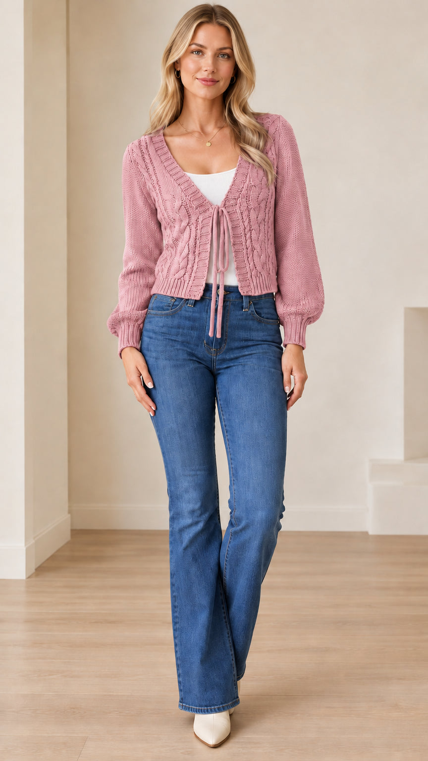 Full front view of a model wearing the dusty pink cable knit tie-front cardigan paired with flare jeans