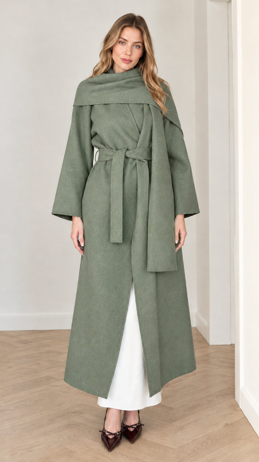 Model wearing sage green belted maxi wrap coat with attached scarf collar